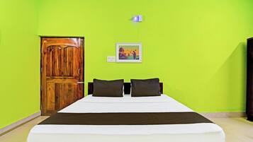 Une pièce avec un lit, une porte en bois, une lampe fixée au mur et un tableau encadré.