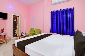Habitación de hotel con cama, escritorio, dos sillas, televisión y ventana con cortinas.