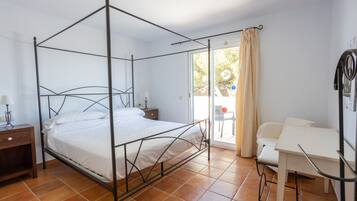 Una cama con dosel con una mesita de noche, un escritorio y una silla en una habitación con piso de baldosas y vistas por un vidrio.