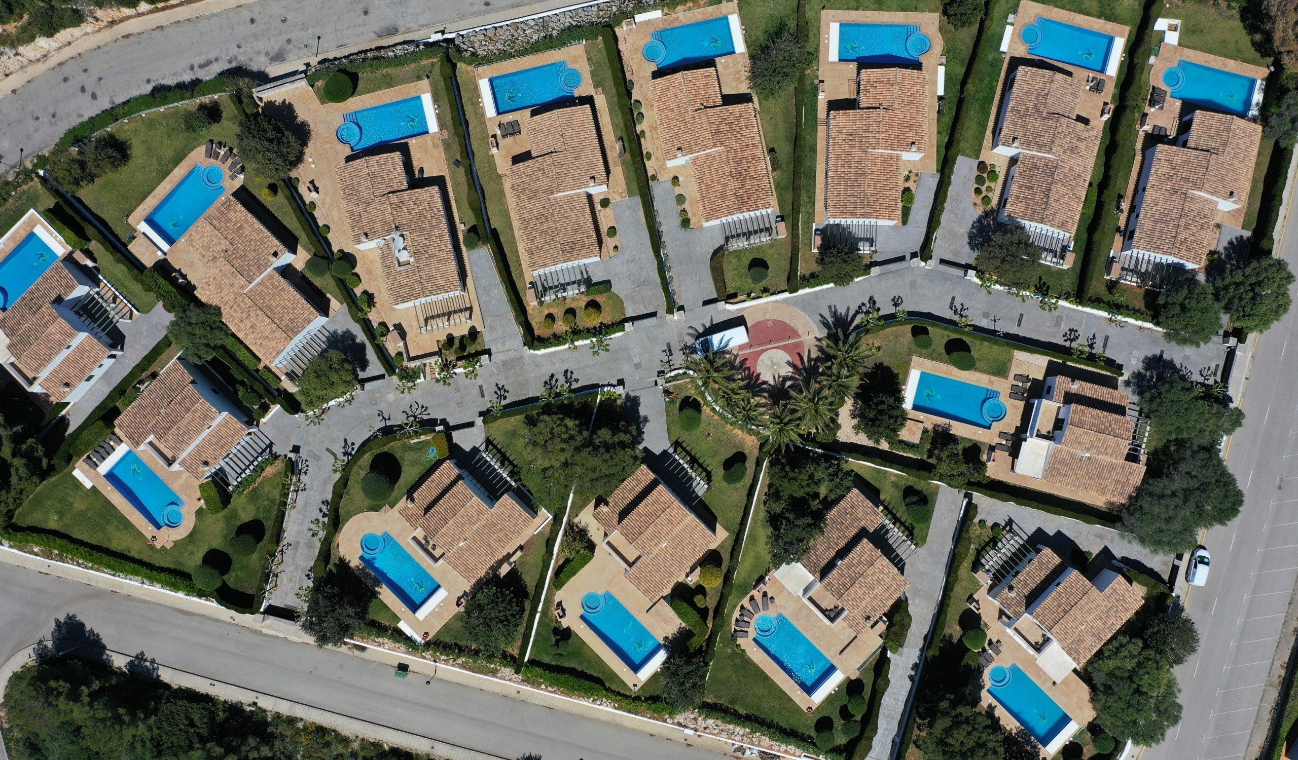 Una zona residencial con varias casas, cada una con piscina y techo de tejas.