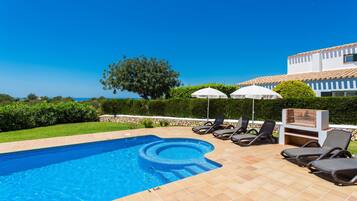 Una piscina con solárium alicatado, sillas de descanso y sombrillas.
