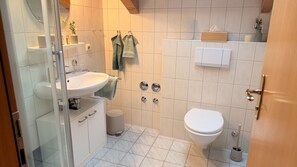 Ein Badezimmer mit weißem Waschbecken, einer Toilette und einer Duschkabine aus Glas.