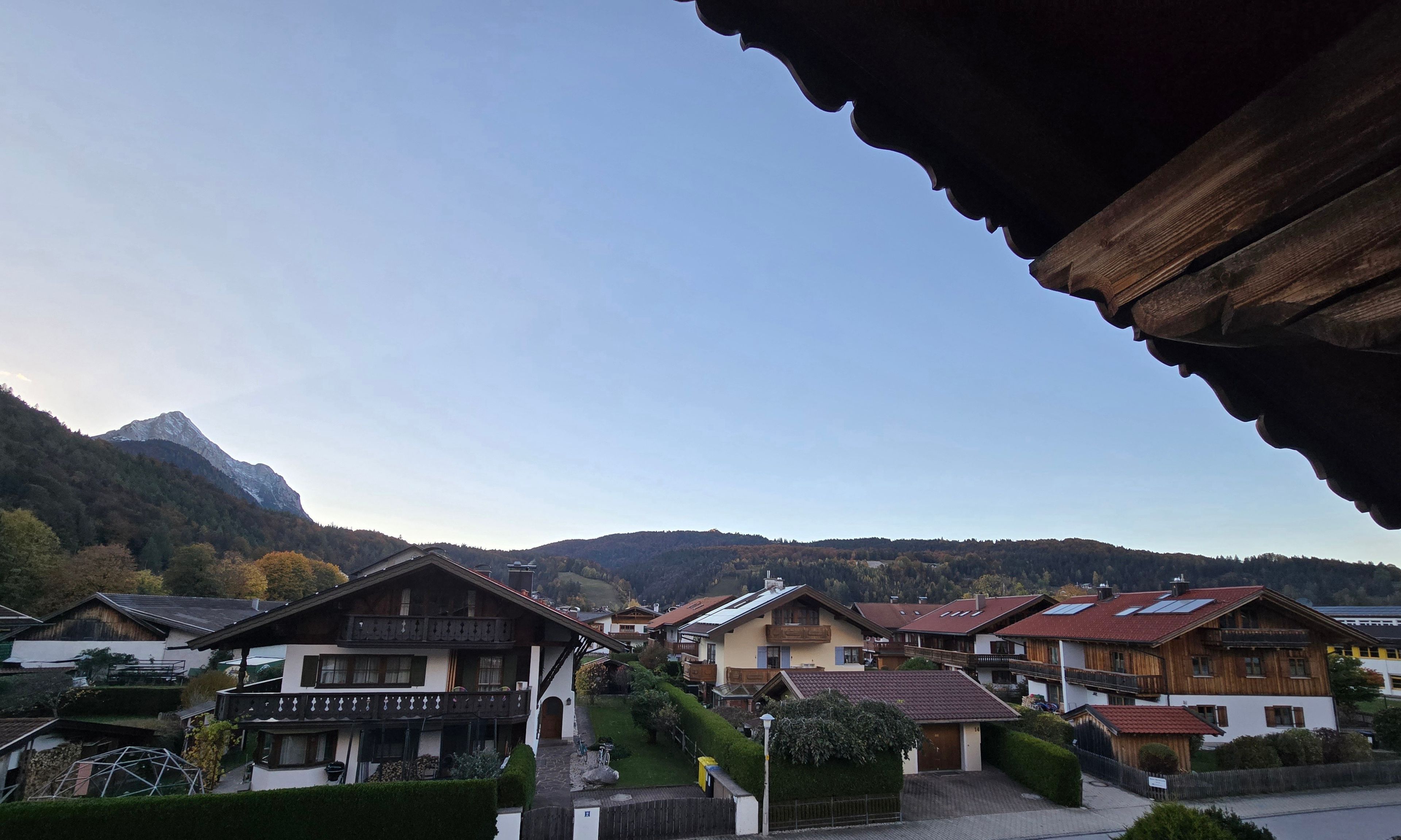 Ein Dorf mit traditionellen Holzhäusern, ein Berg im Hintergrund und ein klarer Himmel.