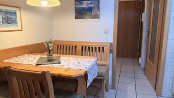 A dining area with a wooden table, chairs, a vase with flowers, a framed picture on the wall, and a poster.
