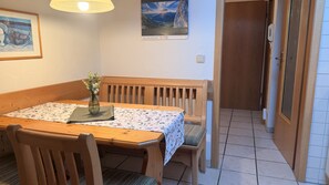 Ein Essbereich mit einem Holztisch, Stühlen, einer Blumenvase, einem gerahmten Bild an der Wand und einem Plakat.