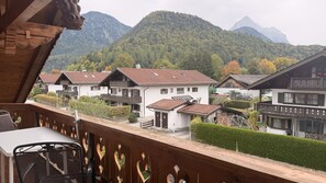 Un edificio de estilo chalé con un balcón, rodeado de abundante vegetación y montañas al fondo.