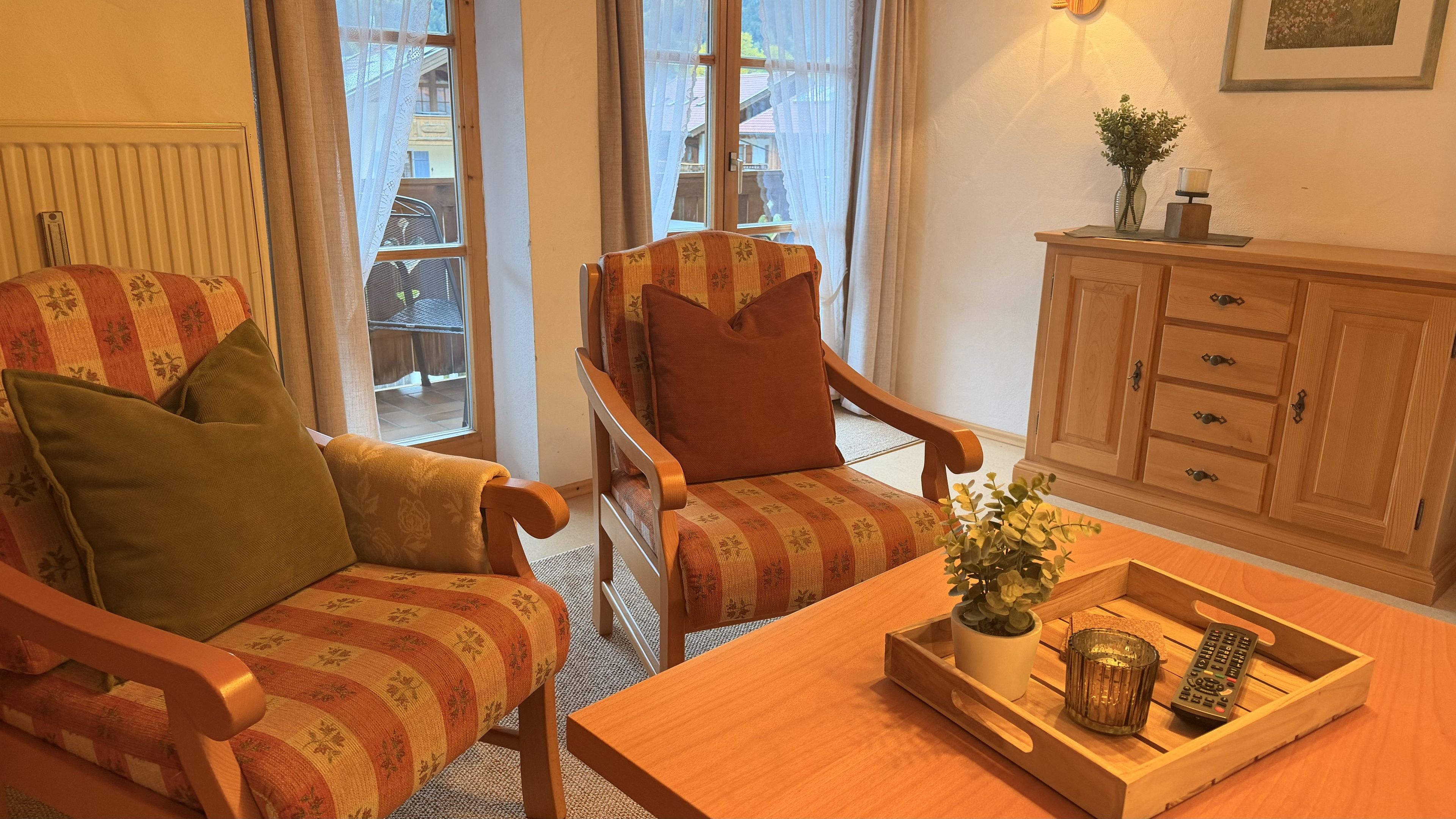 A cozy living room with a wooden armchair, a matching sofa, a wooden coffee table, and a cabinet with drawers.
