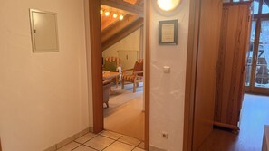 Un pasillo con una puerta de madera que da a una habitación con radiador, un certificado enmarcado en la pared y una ventana con cortinas.
