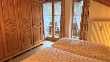 A bedroom with a wooden wardrobe, a bed with floral bedding, and a sliding glass door leading to an outdoor area.
