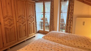 Ein Schlafzimmer mit einem Holzschrank, einem Bett mit floralem Bettbezug und einer Glastür zu einem Außenbereich.