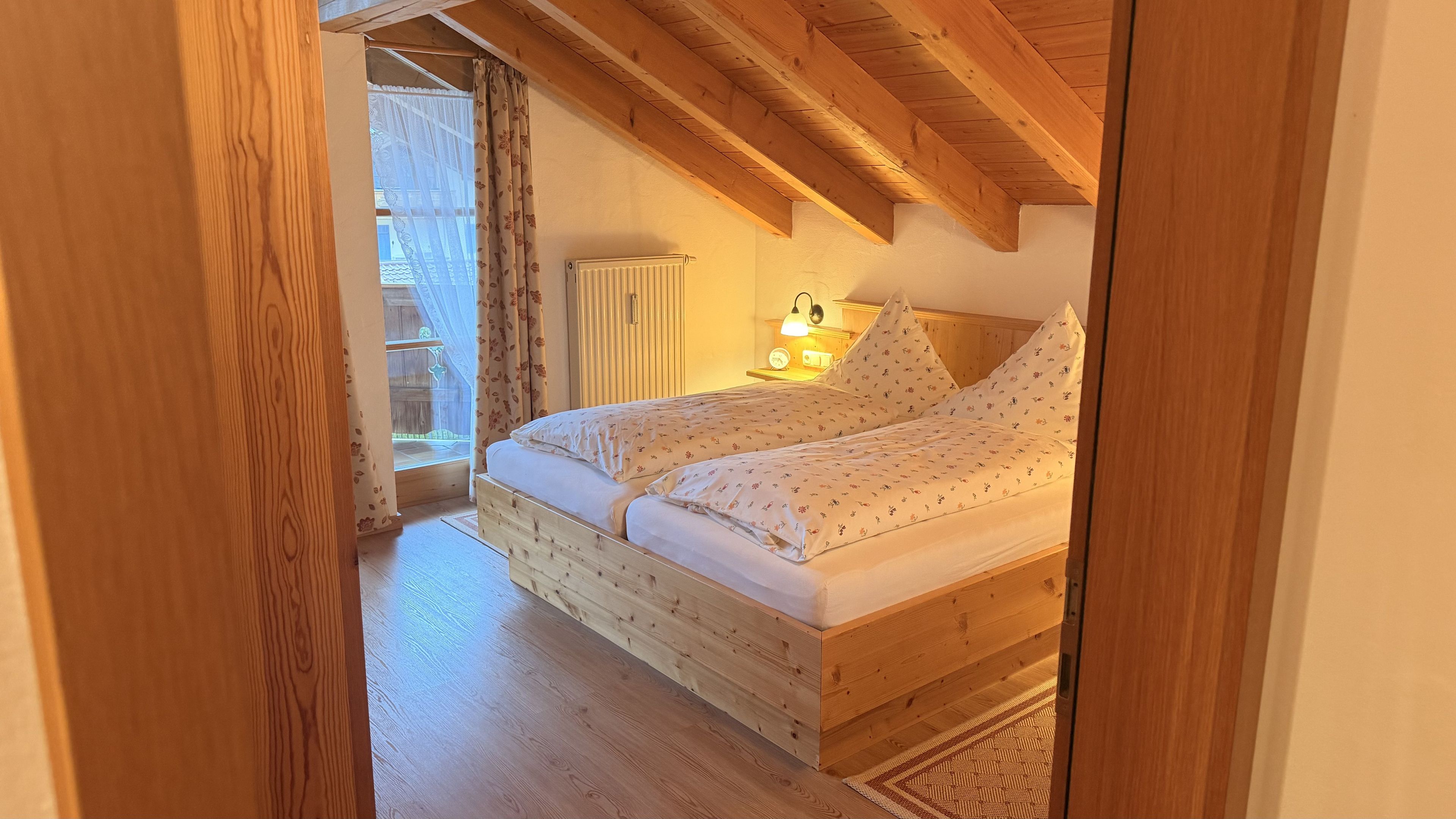 Ein schlicht eingerichtetes Schlafzimmer mit einem Holzbett, einem Nachttisch und einem Fenster mit Vorhängen.