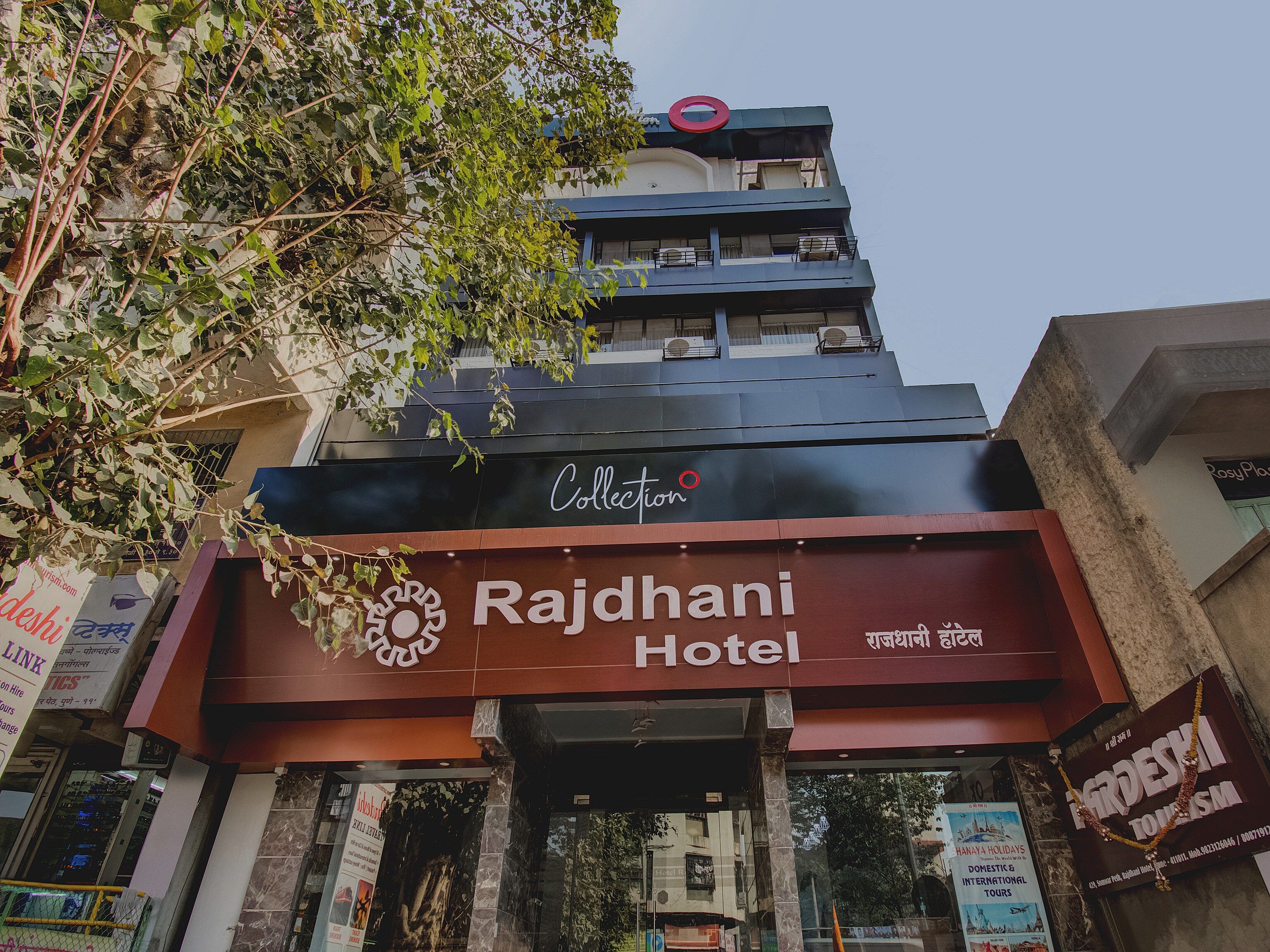 Hotel Rajdhani con un cartel llamativo, un logotipo de la colección en la parte superior y una entrada visible.