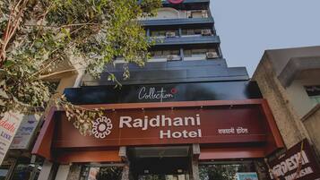 Hotel Rajdhani con un cartel llamativo, un logotipo de la colección en la parte superior y una entrada visible.