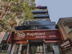 Hotel Rajdhani con un cartel llamativo, un logotipo de la colección en la parte superior y una entrada visible.