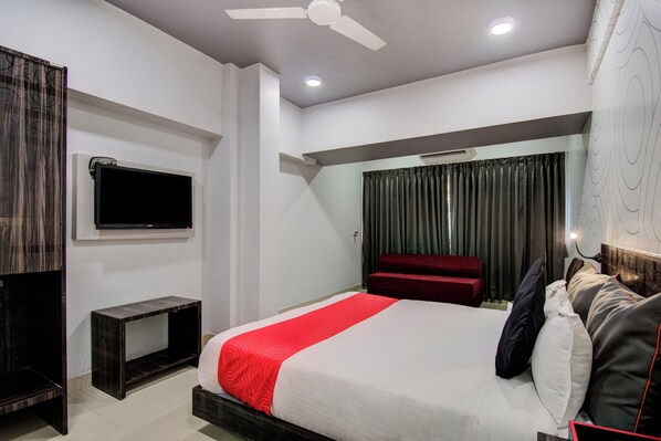 Una habitación de hotel moderna con cama, televisión, ventilador de techo y un amplio ventanal con cortinas.