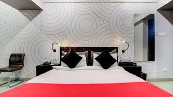 Habitación de hotel con una cama grande, una silla, una mesita de noche con teléfono, un espejo y una pared con un diseño circular.