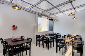 Comedor con varias mesas y sillas, un ventanal con vistas e iluminación colgante.