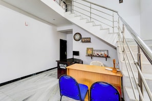 A hotel reception area with a desk, two blue chairs, a staircase, and a clock on the wall. - Hotel O Katpadi Vellore (Vellore)