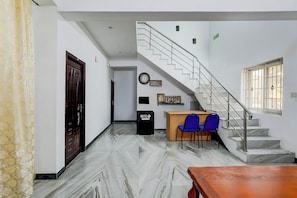 A hotel lobby with a marble floor, a reception desk, two blue chairs, a wooden table, a staircase, and a clock on the wall. - Hotel O Katpadi Vellore (Vellore)