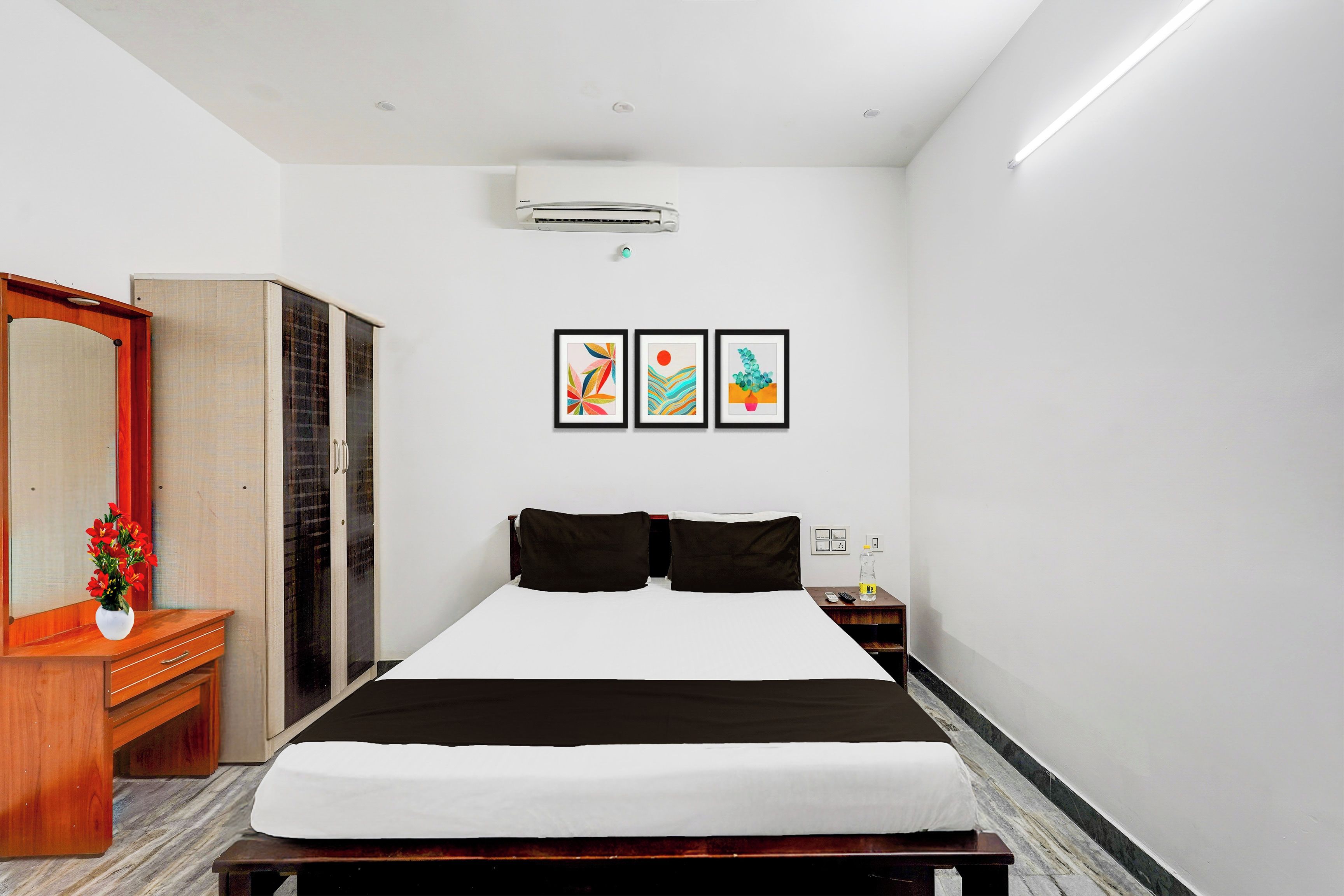 Une chambre d’hôtel avec un lit, une armoire, une table de chevet avec une bouteille et des œuvres d’art murales.
