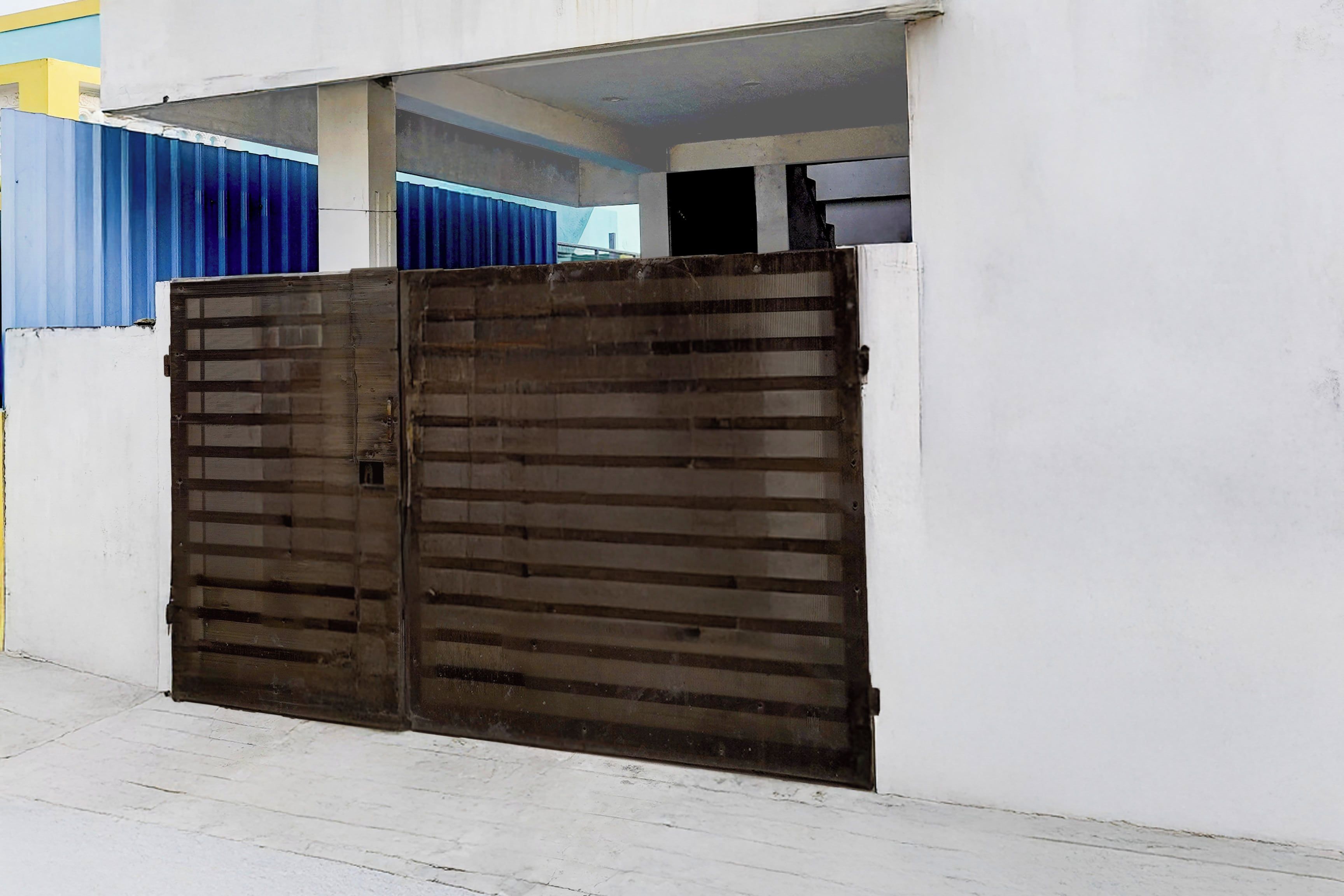 Una reja metálica cerrada frente a un edificio con pared blanca y valla azul y amarilla.