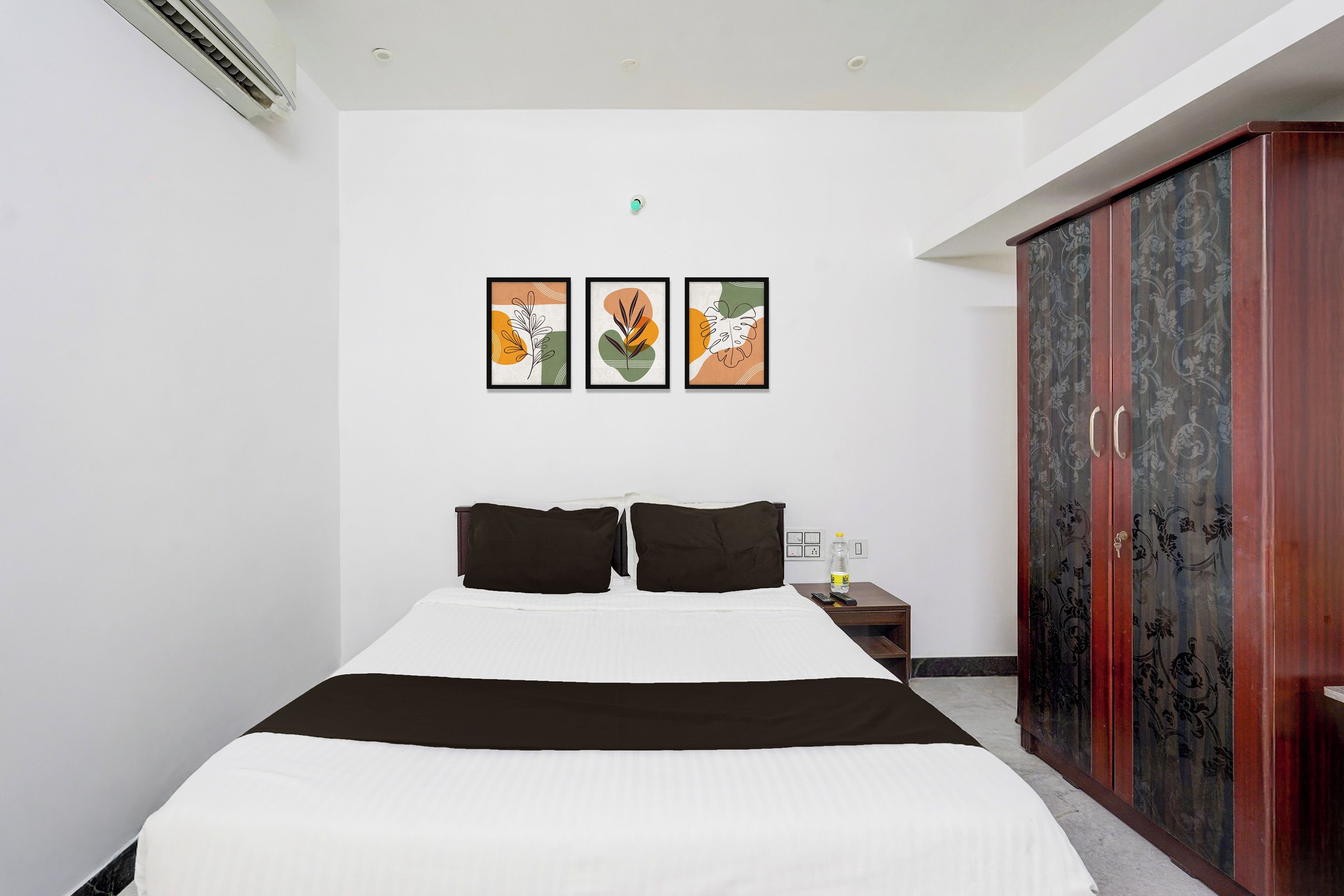A hotel room with a bed, a wardrobe, and two wall-mounted artworks.