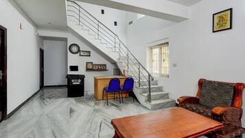 A hotel lobby with a marble floor, a wooden reception desk, blue chairs, a staircase, and a patterned sofa.