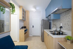 A compact kitchen with a refrigerator, microwave, and sink. There is a coffee maker and a plant on the counter. - Nex One Sena Madureira (São Paulo)