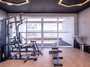Une salle de sport équipée de matériel d’exercice, d’un banc et offrant une vue sur le balcon extérieur.