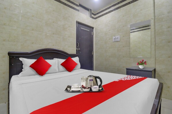 Une chambre d’hôtel avec un lit soigneusement fait, une table de chevet ornée d’un vase de fleurs et un miroir fixé au mur.