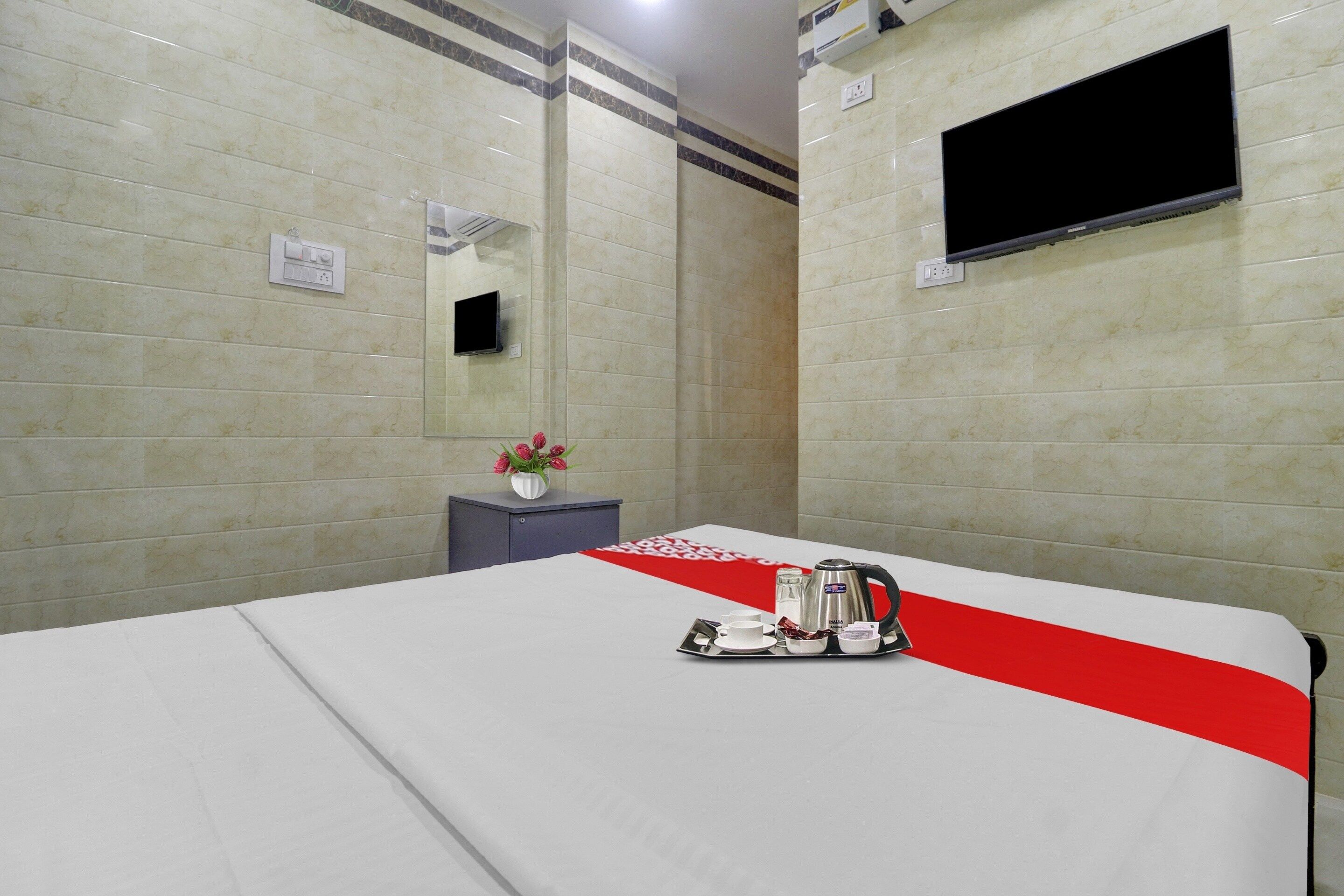 Habitació d'hotel amb un llit, una televisió penjada a la paret, una taula petita amb un ram de flors i un safata amb una tetera i tasses.