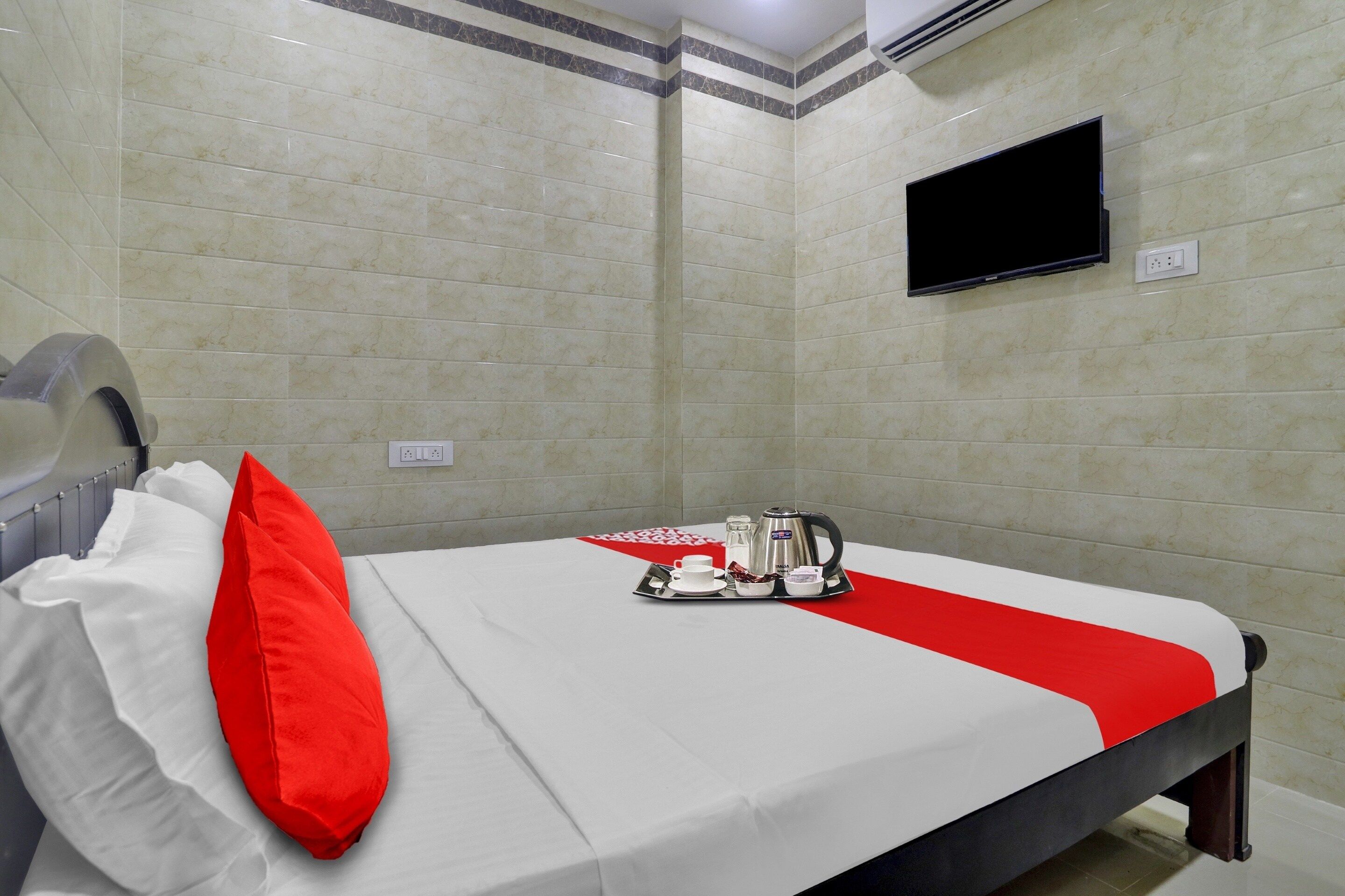A hotel room with a bed, a television mounted on the wall, and a tray with a kettle and cups.