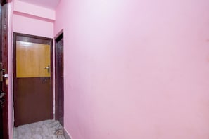 Um corredor estreito com paredes cor-de-rosa e uma porta de madeira.