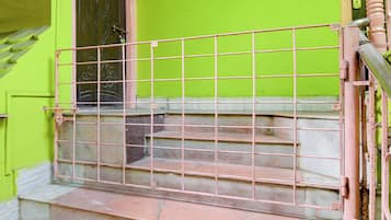 Uma escadaria com corrimão de metal, levando a uma porta com parede verde.