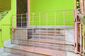 Uma escadaria com corrimão de metal, levando a uma porta com parede verde.