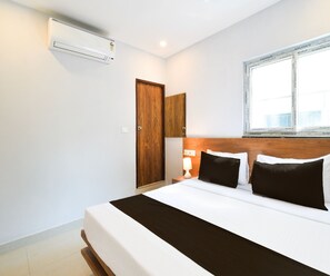 Ein Hotelzimmer mit Bett, Nachttischlampe, Holzschrank und Klimaanlage.