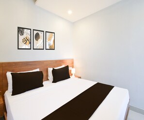 Habitación de hotel con una cama grande, dos almohadas negras, una colcha blanca y un plaid negro. Encima de la cama hay tres obras de arte enmarcadas en la pared.