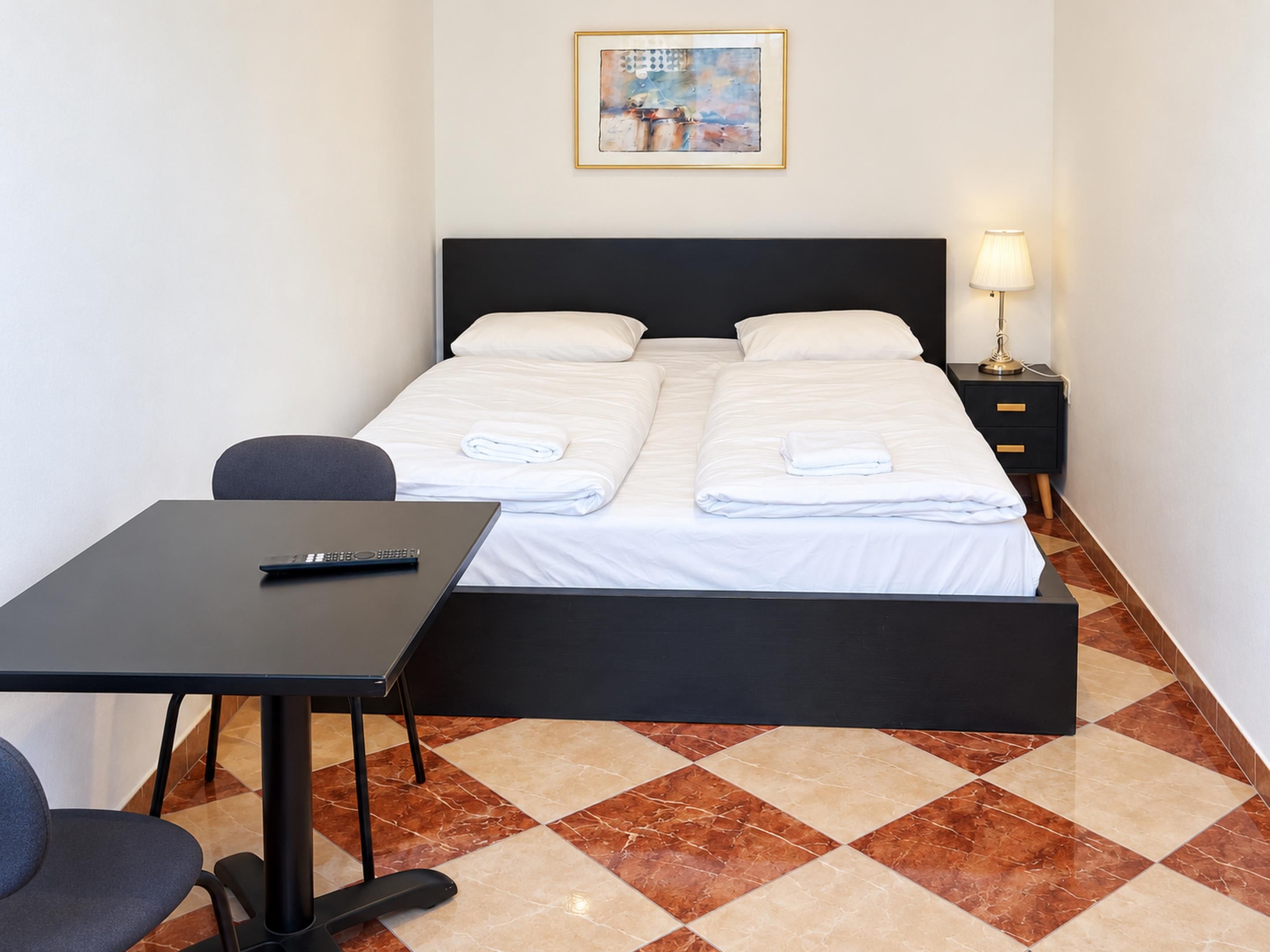 A hotel room with a bed, a desk, a chair, a nightstand, and a lamp.