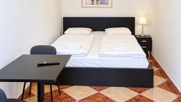 A hotel room with a bed, a desk, a chair, a nightstand, and a lamp.