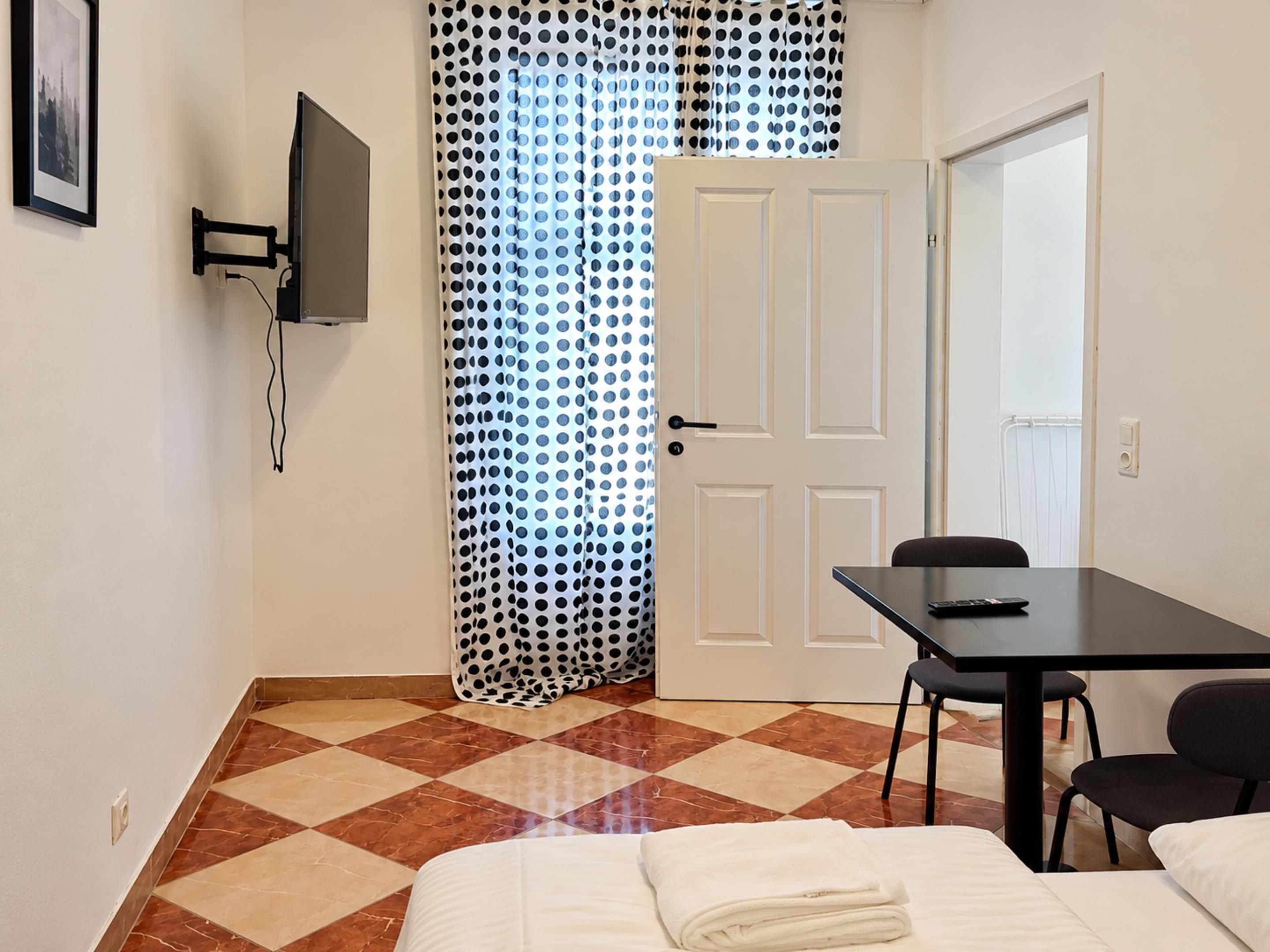 A room with a bed, a desk, a chair, a television, and a door.