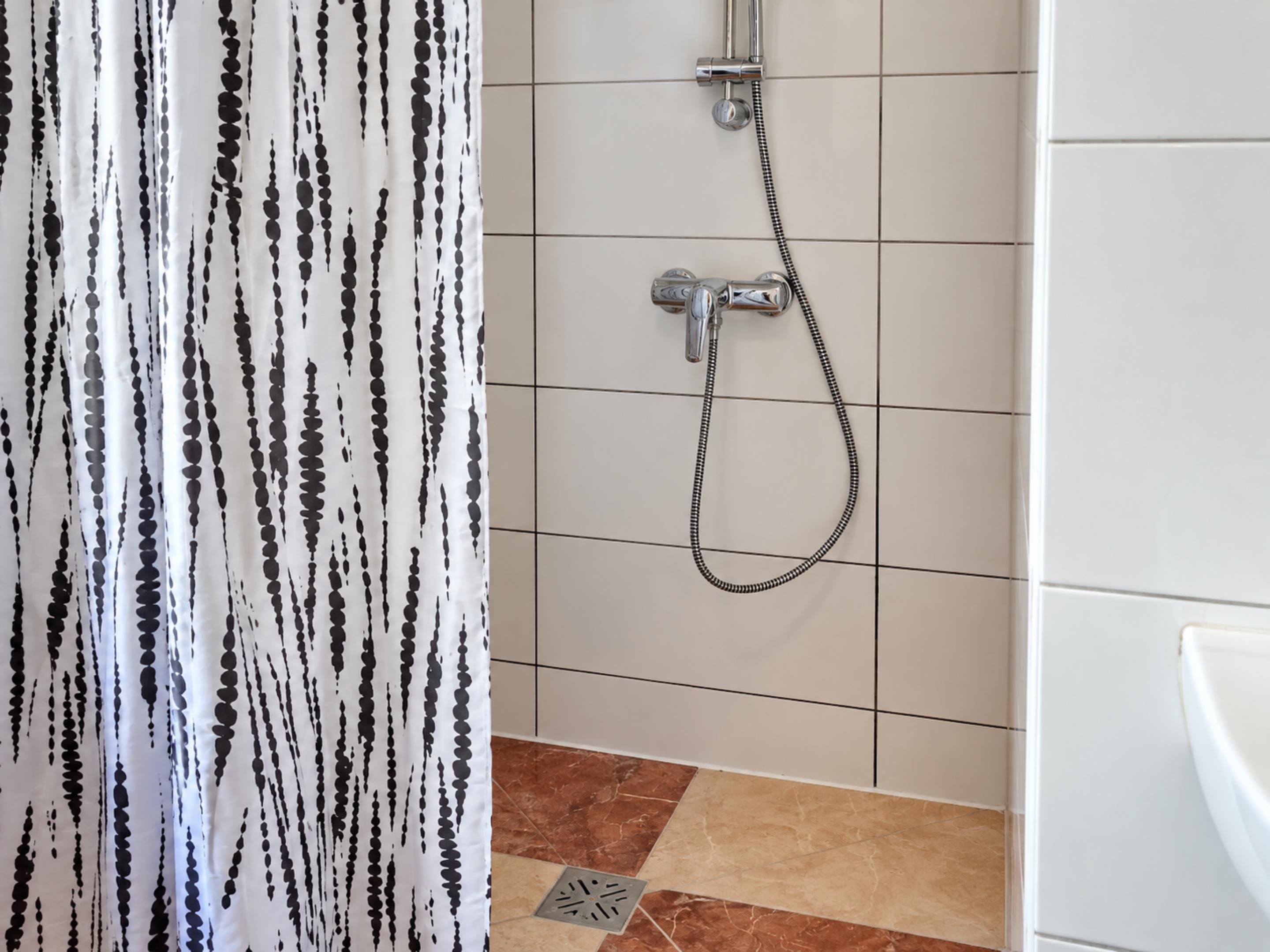 A bathroom with a shower, tiled walls, and a patterned curtain.