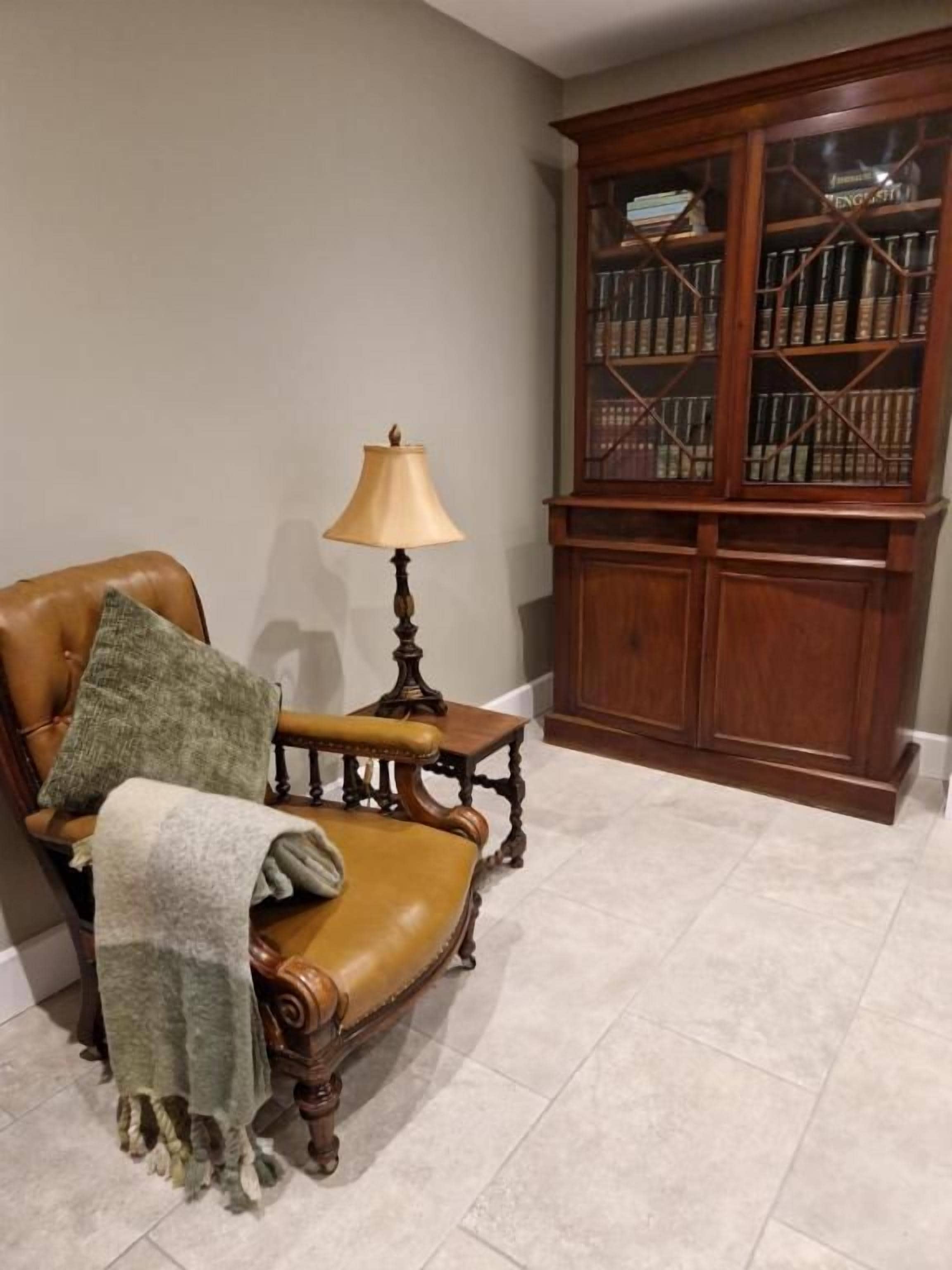 A room with a leather armchair, a small table with a lamp, and a wooden bookcase.