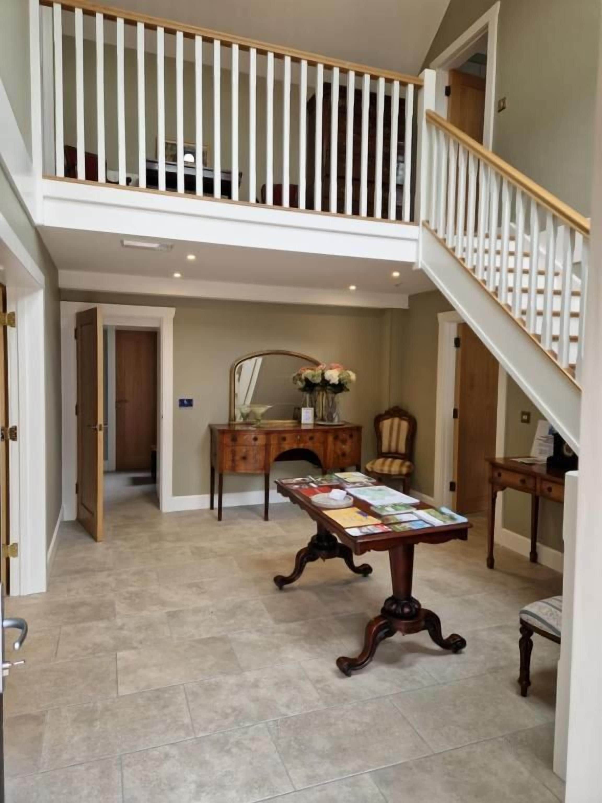 A spacious foyer with a high ceiling, a staircase with white railings, a wooden desk with papers, and a chair.