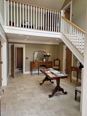 A spacious foyer with a high ceiling, a staircase with white railings, a wooden desk with papers, and a chair. - The Coach House  (Mountmellick)