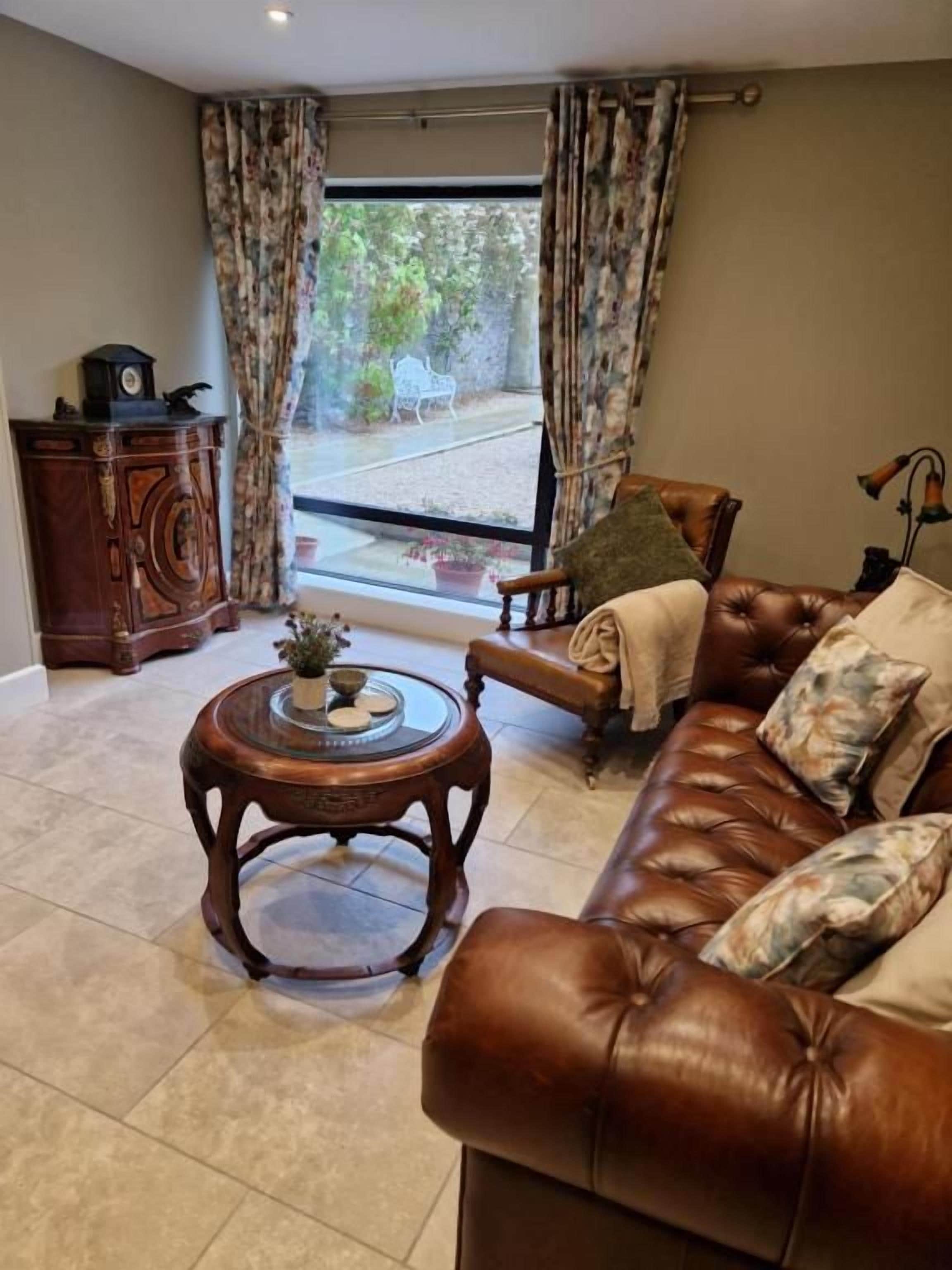 A living room with a leather sofa, a round wooden coffee table, and a view through a glass door to the outside.