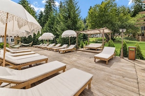 A wooden deck with lounge chairs and umbrellas, surrounded by greenery. - Hotel Forestia (Borovets)