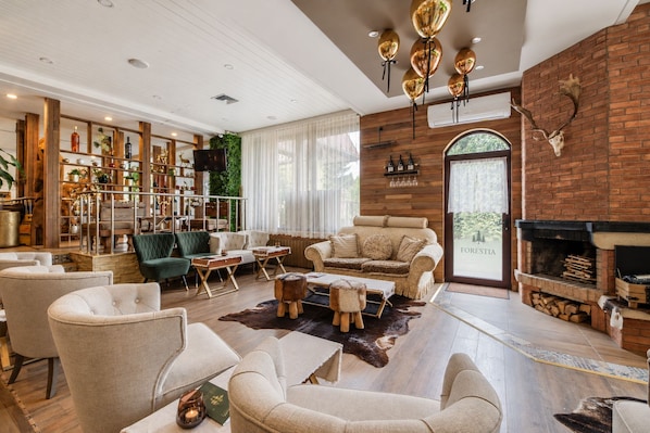 A spacious living room with a fireplace, leather sofas, and a rustic brick wall. - Hotel Forestia (Borovets)