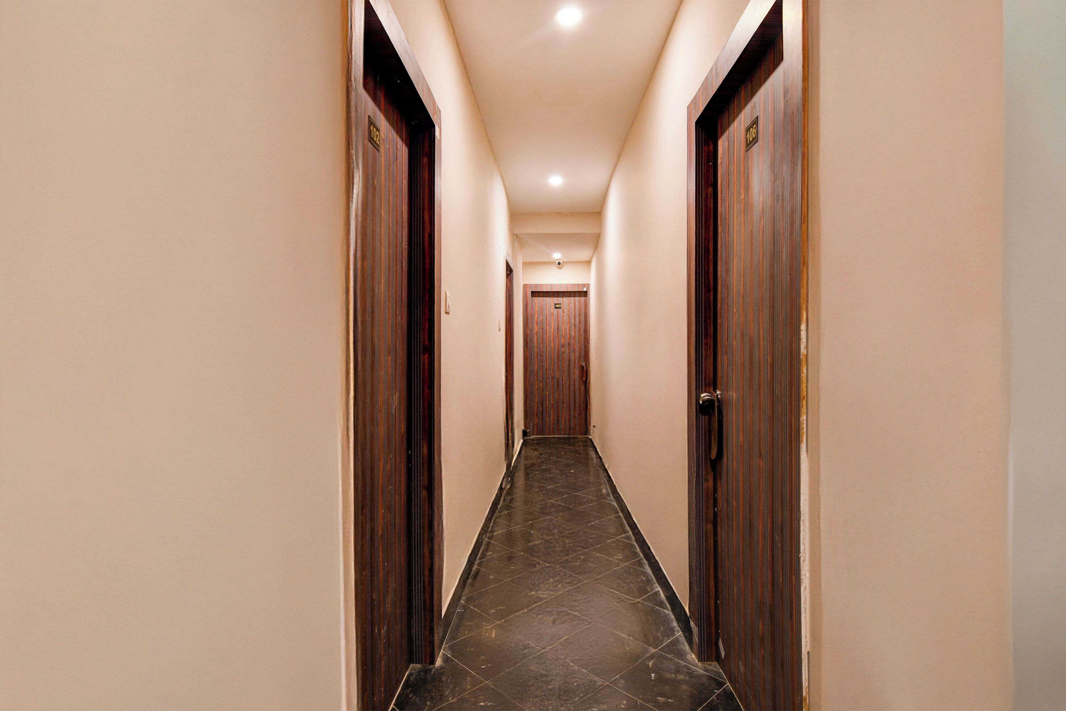 Un pasillo de hotel con puertas de madera a ambos lados, suelo de baldosas y pared de color claro.