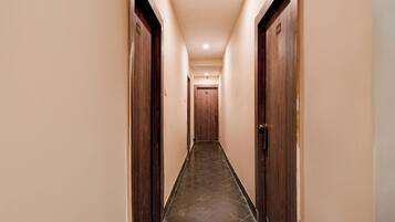 Un pasillo de hotel con puertas de madera a ambos lados, suelo de baldosas y pared de color claro.