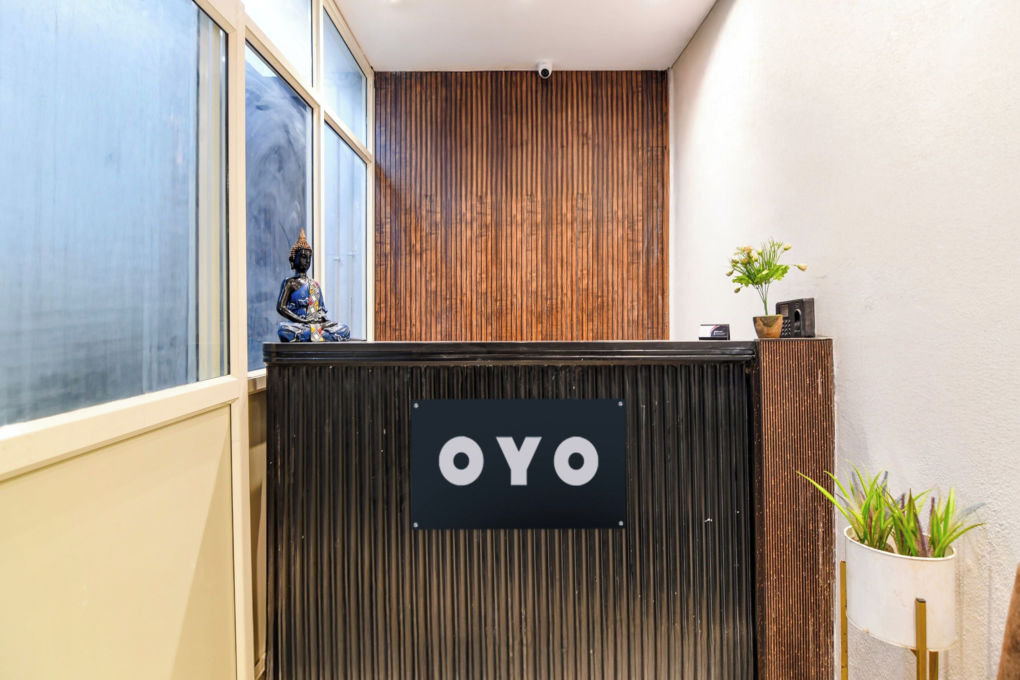 Un taulell de recepció amb un cartell que diu 'OYO' a un vestíbul modern d'hotel amb una paret de fusta i una planta en test.